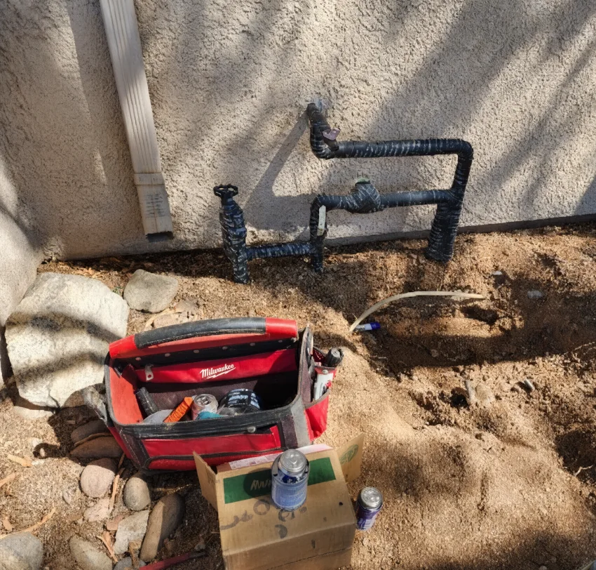 An irrigation pipe installed to the side of the wall, with tools on the ground